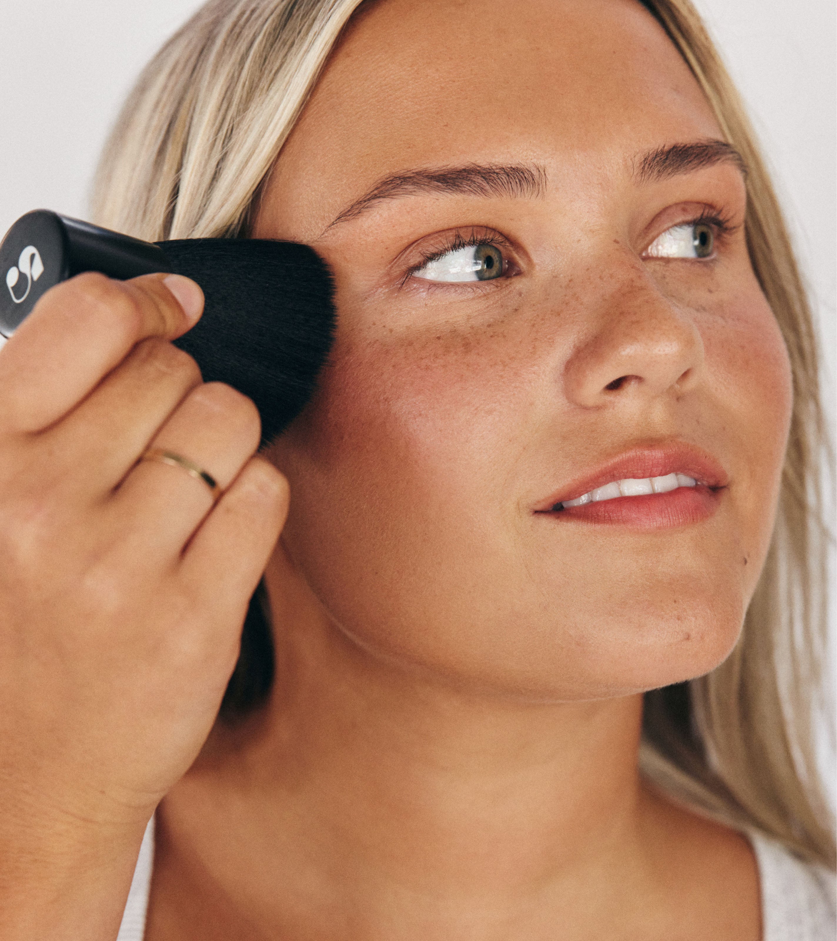 Closeup of model using Saltyface Brush No. 1 to apply Tanning Water on her face.